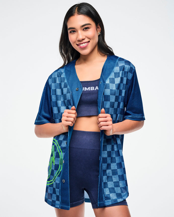 Female model wearing an unbuttoned blue checkered jersey, paired with a matching blue denim bra with white Zumba text and blue denim shorts.