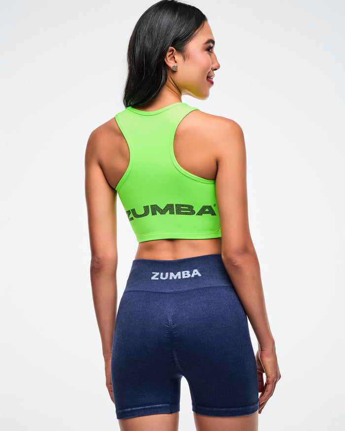 Back view of a neon green crop tank with “Zumba” text along the bottom, paired with blue corduroy biker shorts featuring white “Zumba” text on the waistline, worn by a female model.