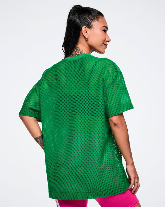 Back view of a female model wearing a green mesh Zumba top on a white background.