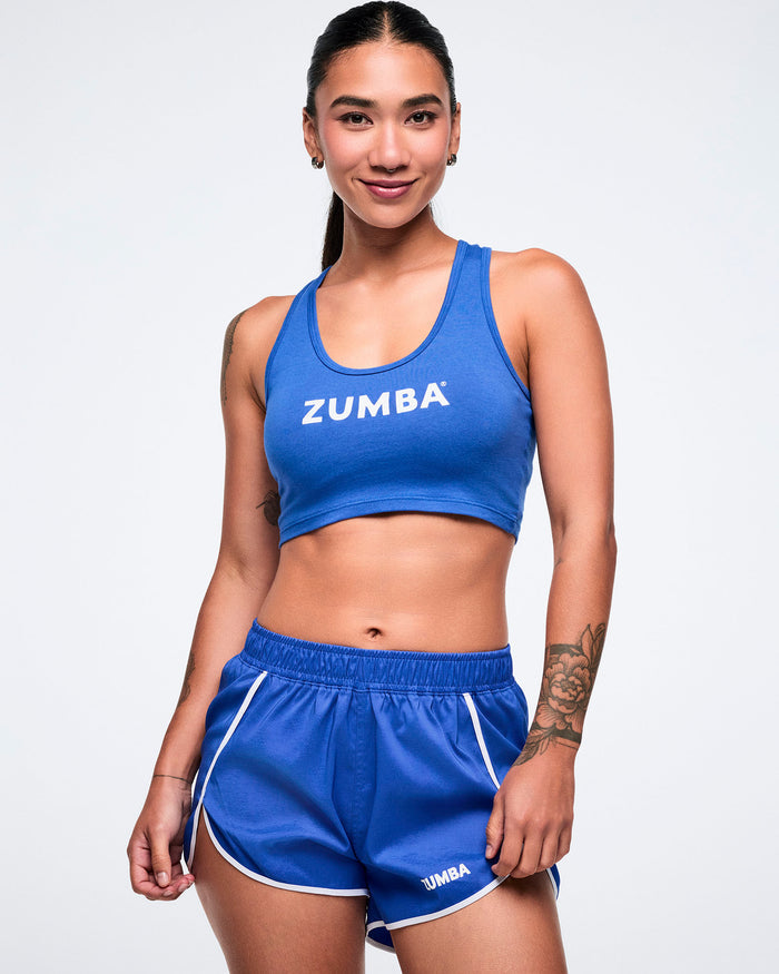 Female model wearing a blue Zumba crop racerback and blue shorts.
