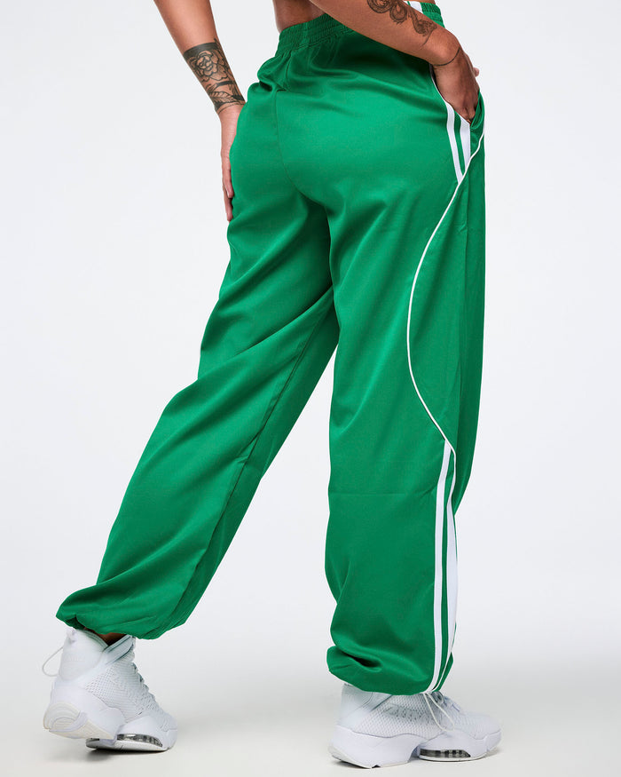 Back view of a female model wearing green Zumba curvy track pants with white stripes and white shoes.