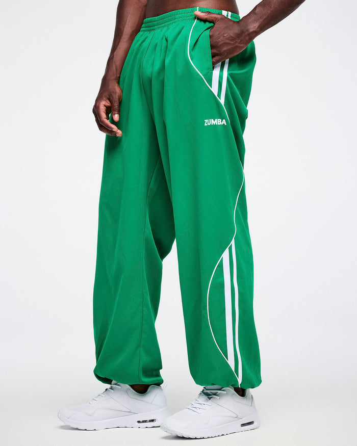 Male model with his hand in the left pocket of the green Zumba curvy track pants with white stripes.