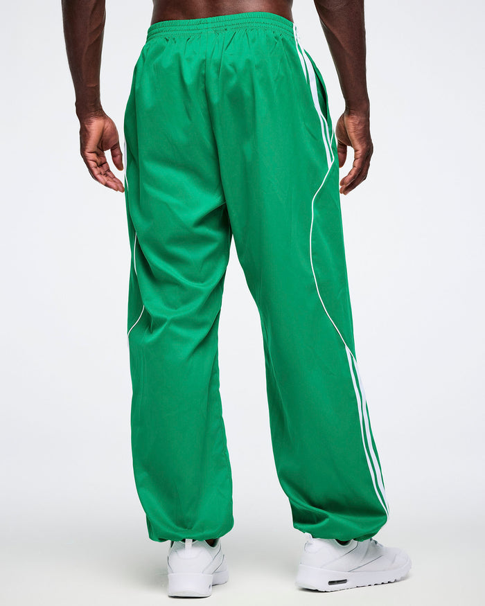 Male model posing with a back view of the green Zumba curvy track pants with white stripes.