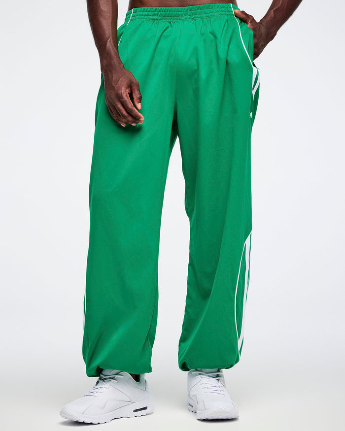 Male model in green curvy track pants with a white stripes and white shoes.