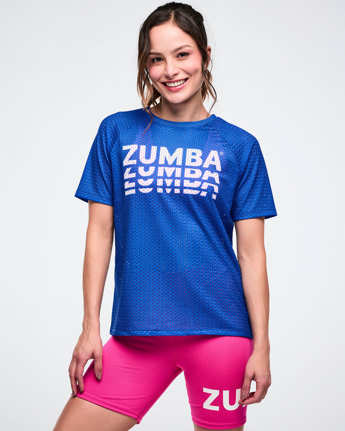 Female model wearing a blue Zumba mesh top and pink shorts on a white background.