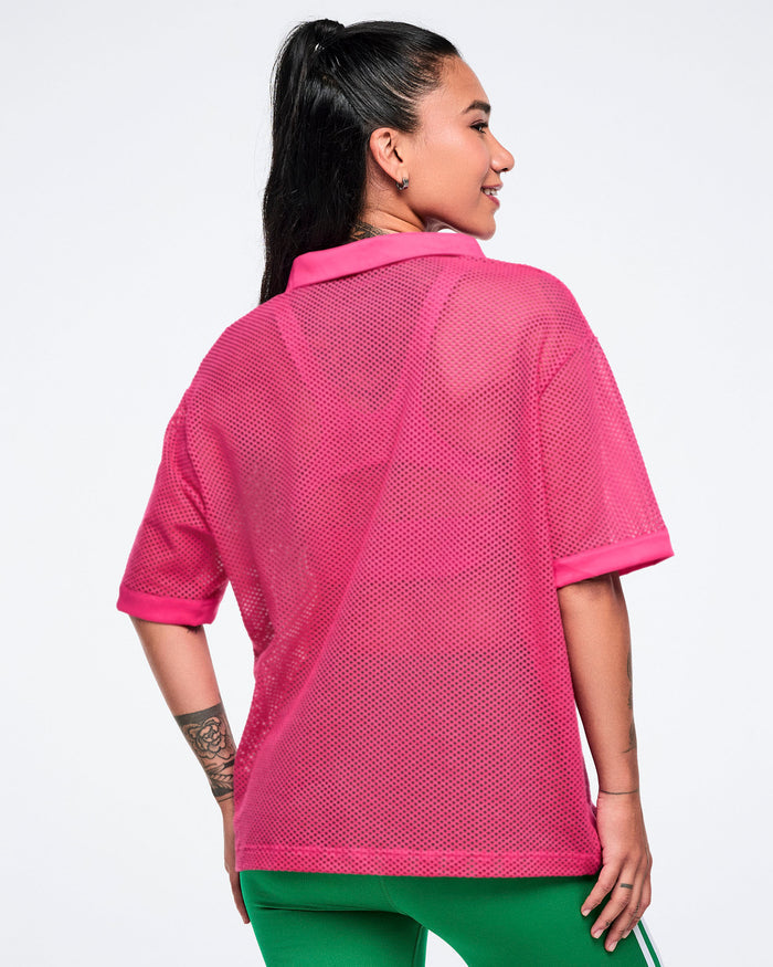 Back view of female model wearing a pink mesh polo with green pants.