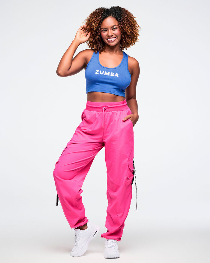 Female wearing a blue Zumba racerback top and pink cargo pants against a white background.
