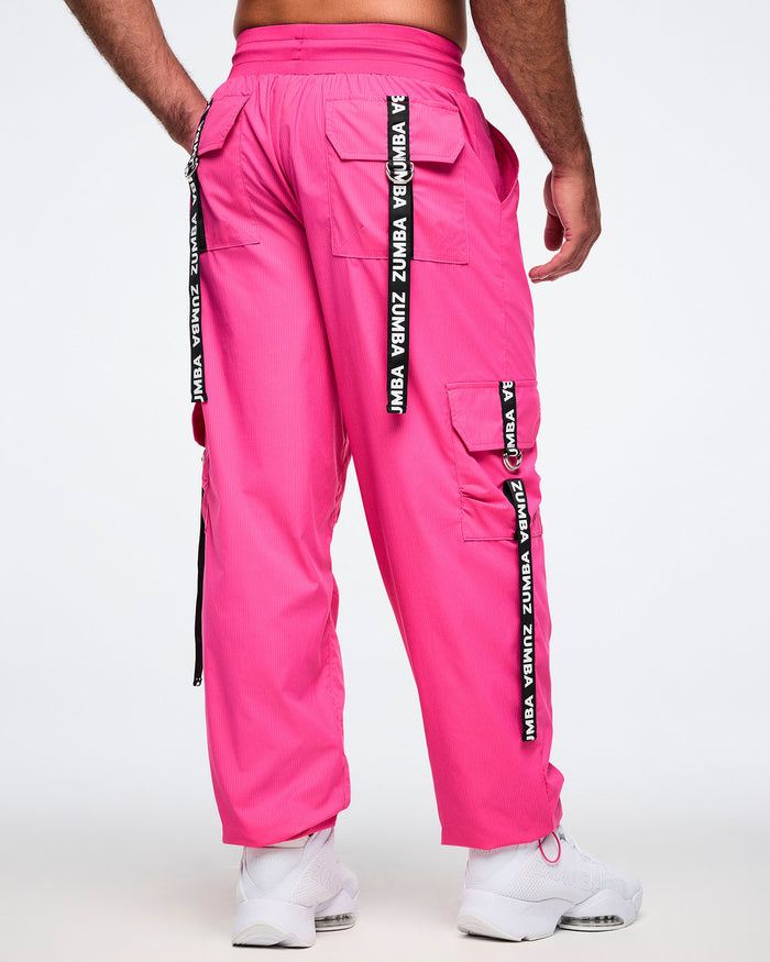 Back view of the pink cargo pants with white'Zumba' branding on the back ribbons on each pocket, worn by a male model.