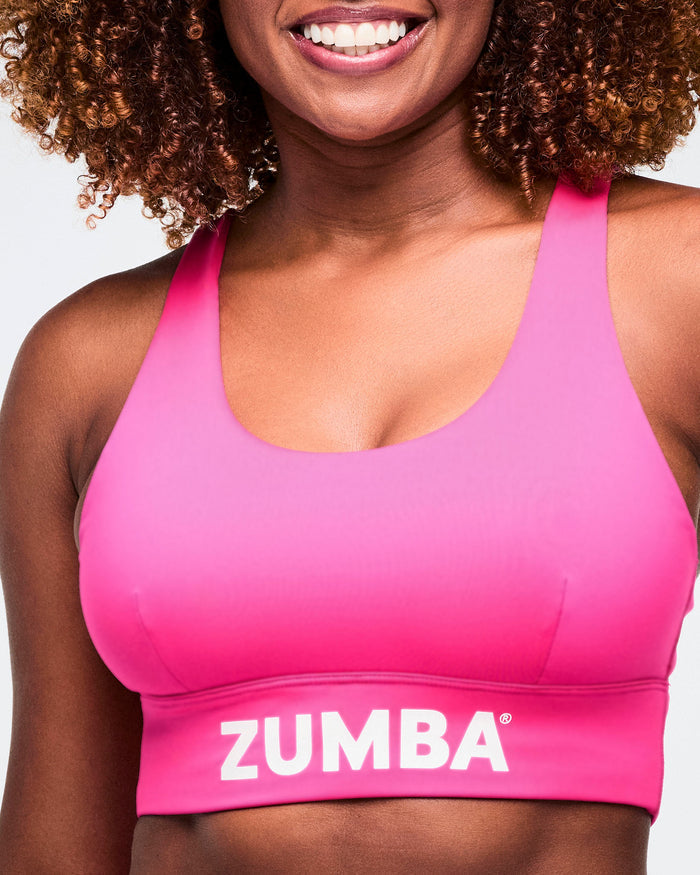 Close-up of a pink scoop neck bra with Zumba on the bottom band, worn by a female model.
