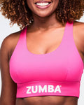 Close-up of a pink scoop neck bra with Zumba on the bottom band, worn by a female model.