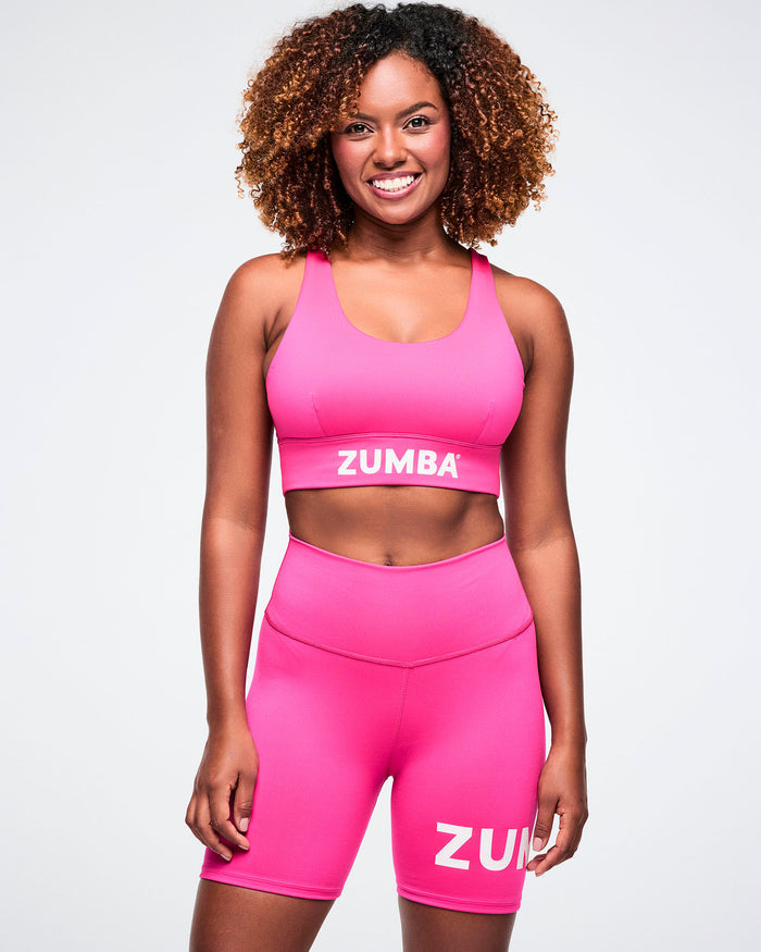 Female model wearing a pink scoop bra and pink biker shorts on a white background.