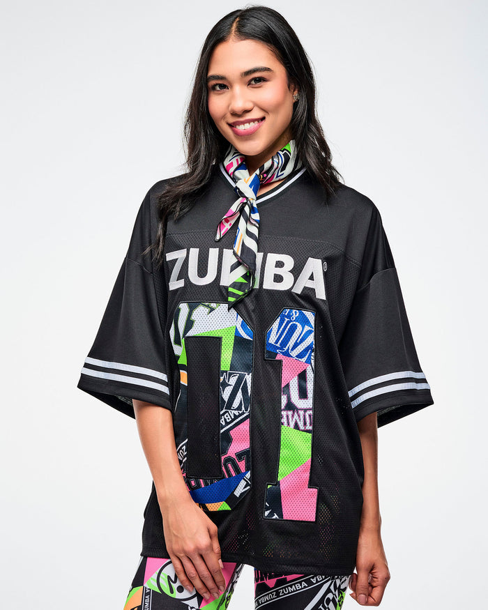 Female model wearing a bandana around her neck and a black graphic top with colorful patterns and text on a white background.
