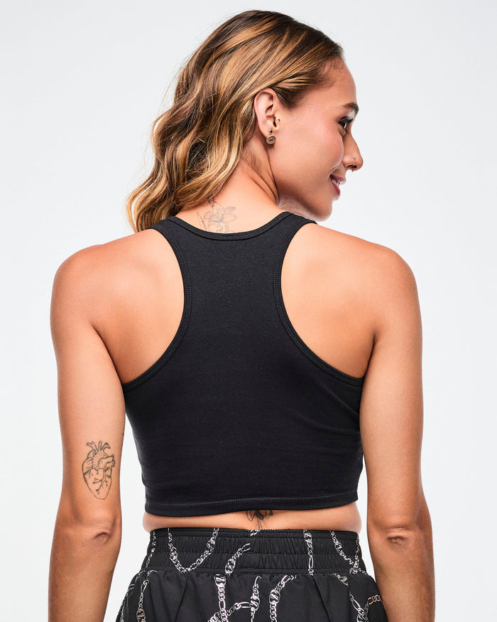 Back view of a female model wearing a black Zumba sports bra and black pants with white patterns on a light background.