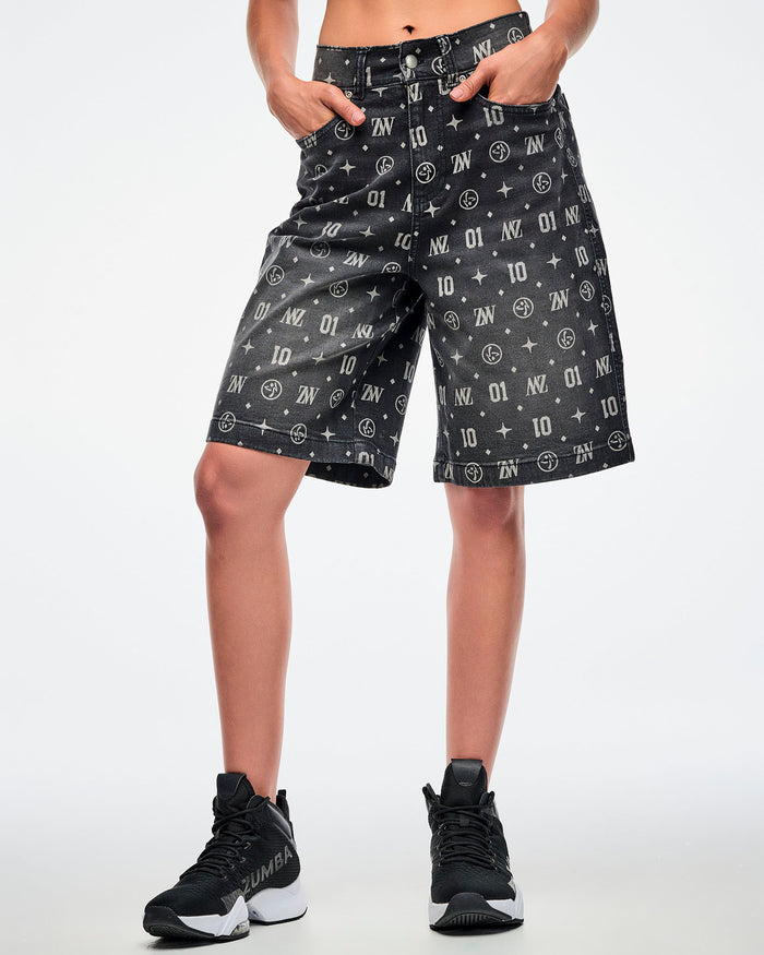 Female model with hands in the pockets of black denim jorts featuring patterned ZW, “01,” stars, dots, and Zumbito motifs, paired with black-and-white shoes.