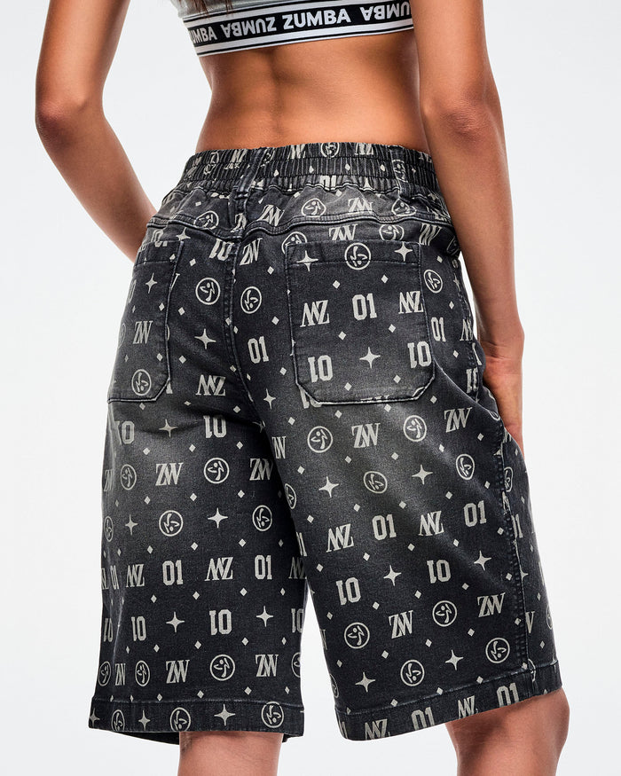 Back view of a female model wearing black denim jorts, showcasing two functional back pockets and patterned ZW, “01,” stars, dots, and Zumbito motifs, paired with black-and-white shoes.