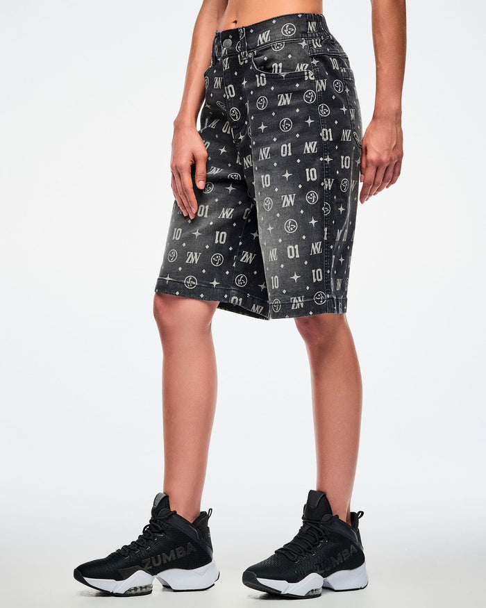 Side view of a female model wearing black denim jorts with patterned ZW, “01,” stars, dots, and Zumbito motifs, paired with black-and-white shoes.
