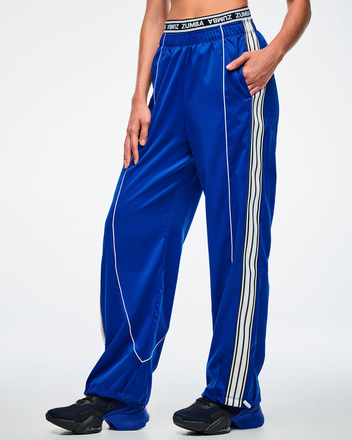 Female model with hand in her pocket, wearing blue woven pants with white stripes paired with blue and black shoes.