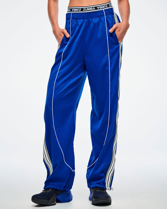Female model with both hands in her pocket, wearing blue woven pants with white stripes paired with blue and black shoes.