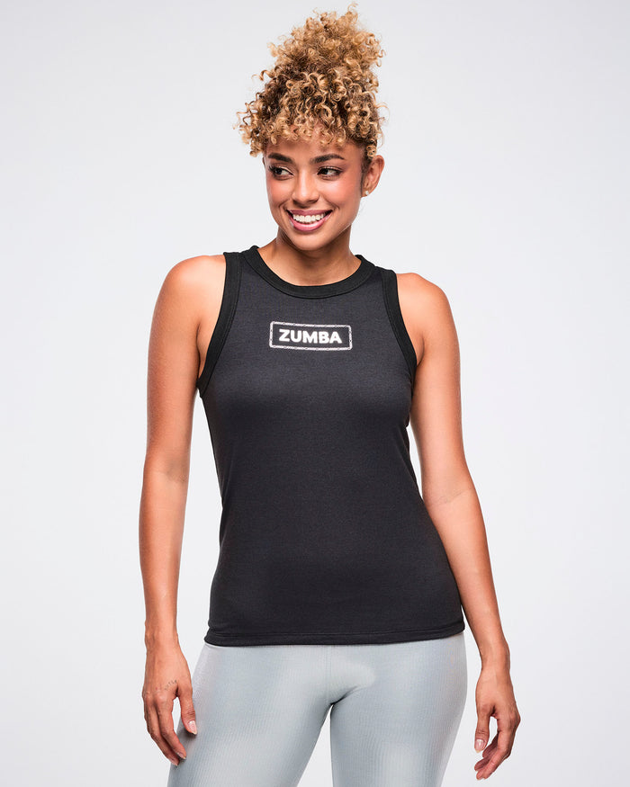 Female model wearing a black tank top with a silver 'Zumba' logo on the chest, paired with silver biker shorts.
