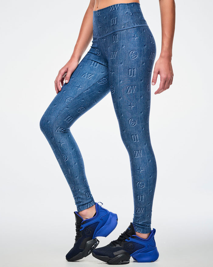 Female model in blue denim-print leggings with “ZW, 01, dots, Zumbito” pattern, blue-black shoes, on a white background.