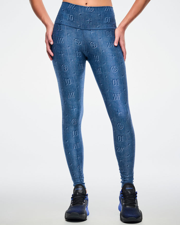 A female model stands with hands on hips, wearing denim-print leggings with “ZW, 01, dots, Zumbito” and a rear patch, paired with blue-black shoes.