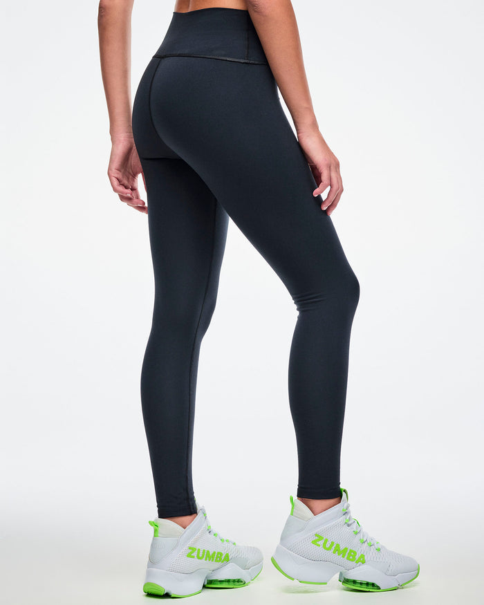 Back view of a female model wearing black Zumba leggings paired with green-and-white shoes.