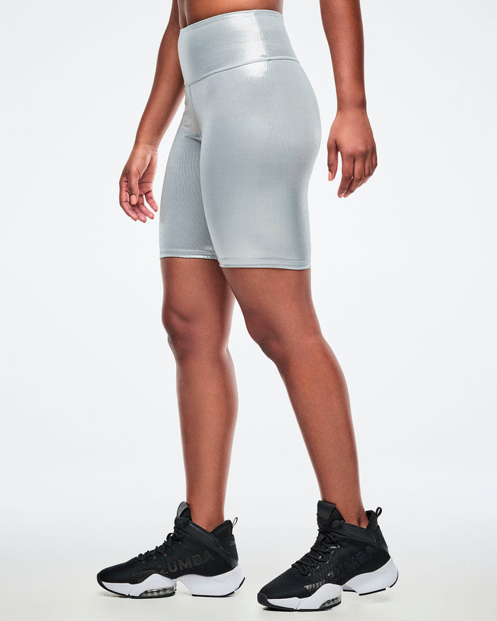Female model wearing silver ribbed biker shorts paired with a black and white shoes on a white background.