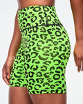 Close-up side view of a female model wearing neon green biker shorts with black leopard print pattern on a white background.
