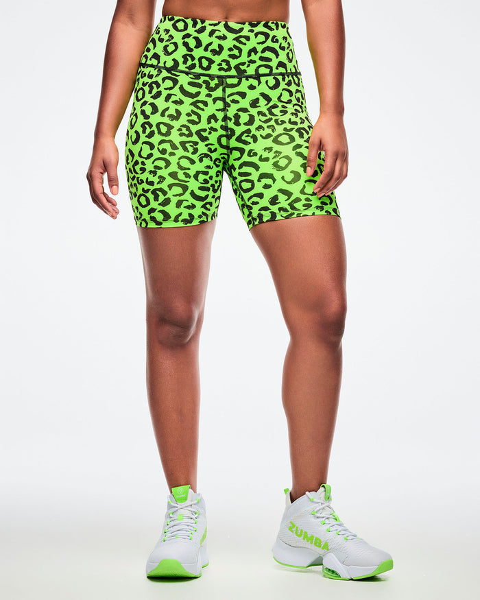 Female model wearing neon green biker shorts with black leopard print pattern paired with green and white shoes.