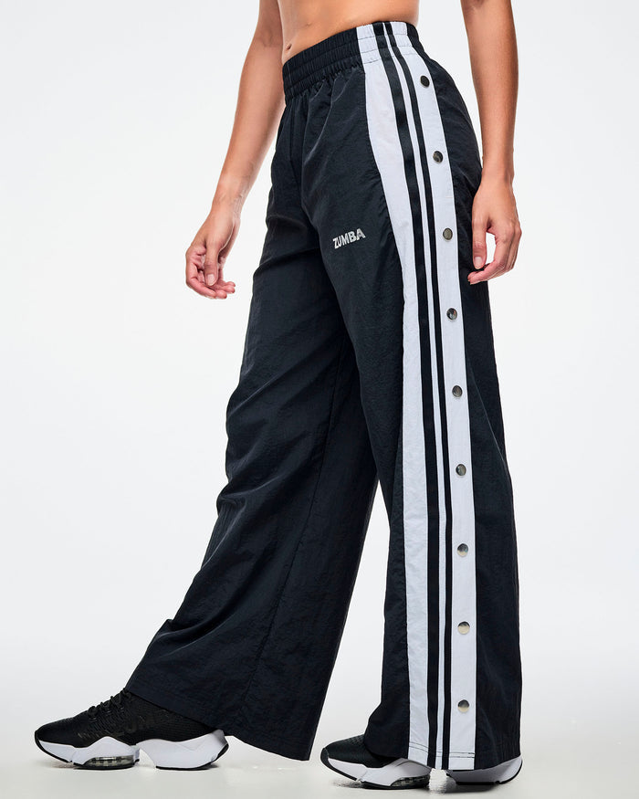Female model wearing black pants with white stripes on the side with side snaps and paired with black and white shoes.