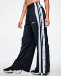 Female model wearing black pants with white stripes on the side with side snaps and paired with black and white shoes.