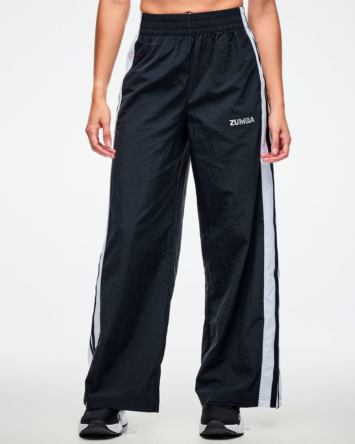 Front view of black track pants with white side stripes and “Zumba” in white on the upper left leg.