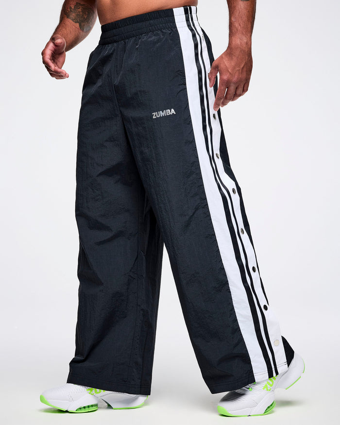 Male model wearing black Zumba pants with white stripes on a white background.