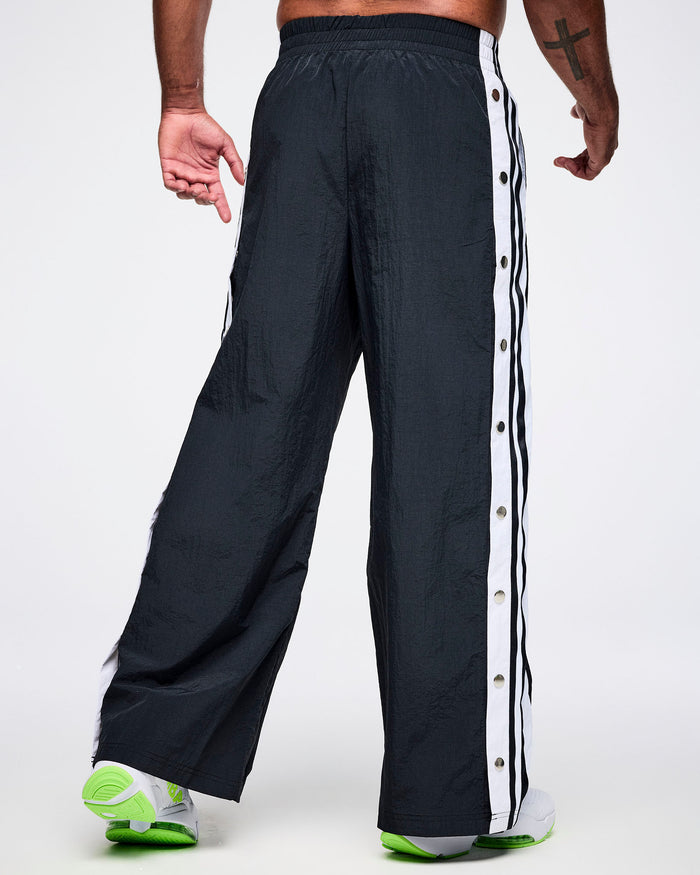 Back view of a male model wearing black Zumba pants with white stripes on a white background.