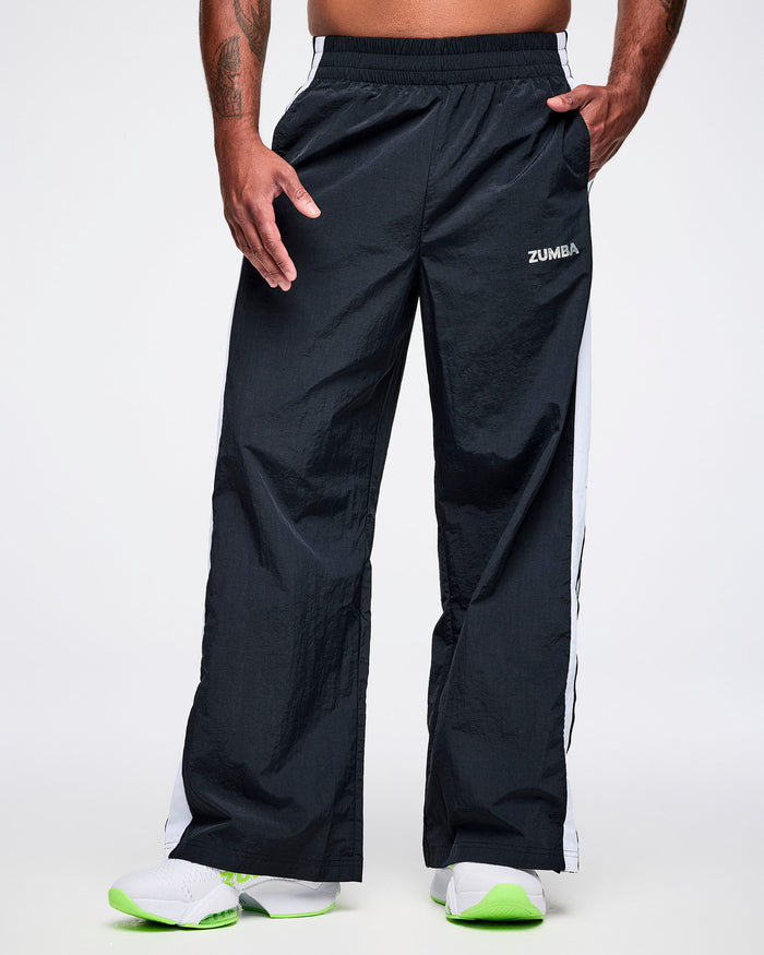 Front view of a male model wearing black Zumba pants with white stripes and white Zumba on the upper left leg.