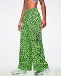 Female model wearing high-waisted neon green cargo pants with black leopard print, elastic waistband, and side cargo pocket featuring a vertical black tape that reads “Zumba.” Styled with white athletic sneakers accented in matching neon green all on a white background.