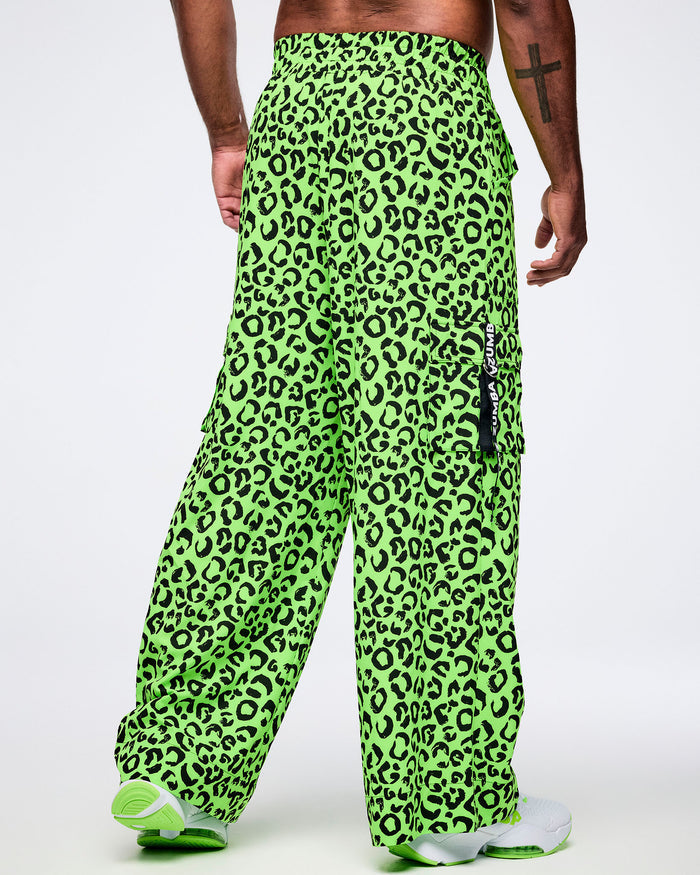 Back view of a male model wearing bright green leopard print pants with a visible brand logo on a white background.