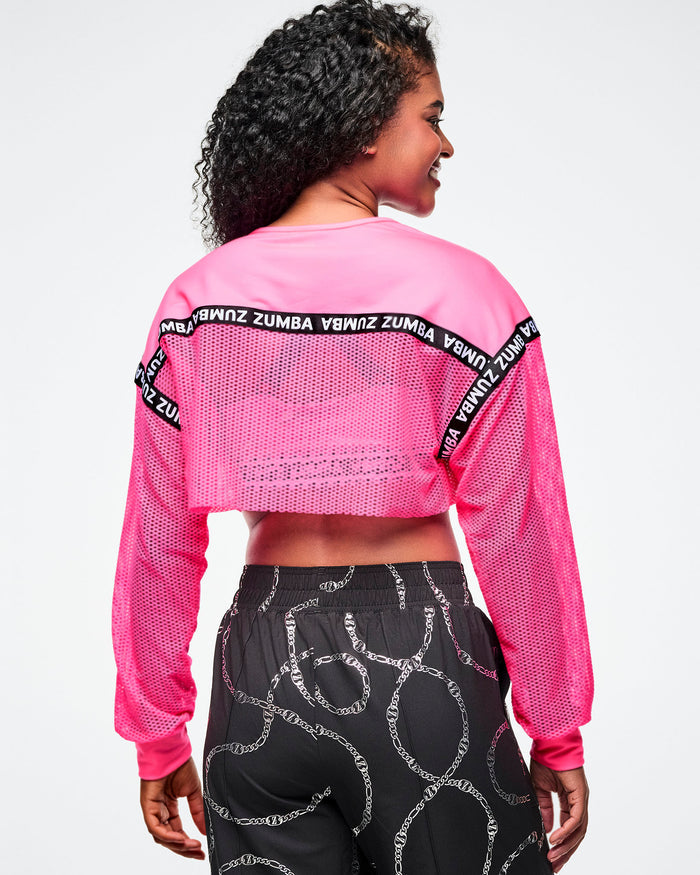 Back view of a female model wearing a pink Zumba crop top and black patterned pants on a white background.