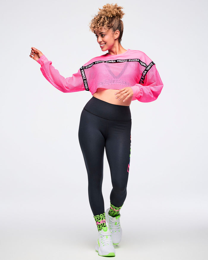 Female model dancing with swinging arms, wearing a pink cropped top, black leggings, green leopard-print socks, and green-and-white shoes.