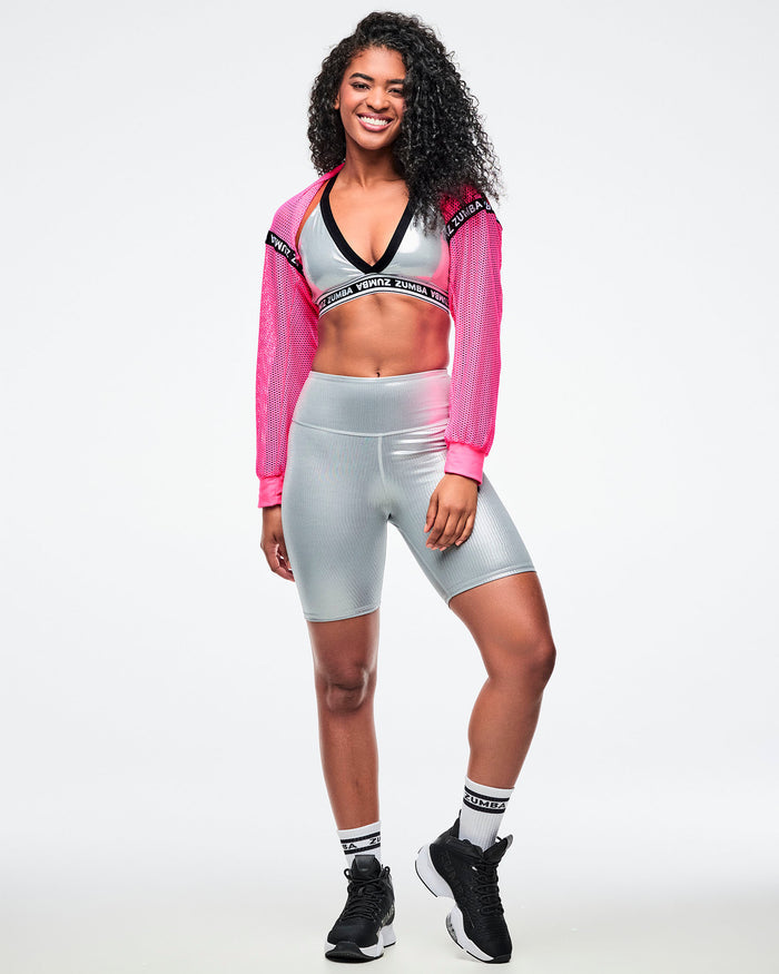 Female model wearing a pink cropped top, revealing a silver bra with matching biker shorts, paired with black-and-white socks and shoes.