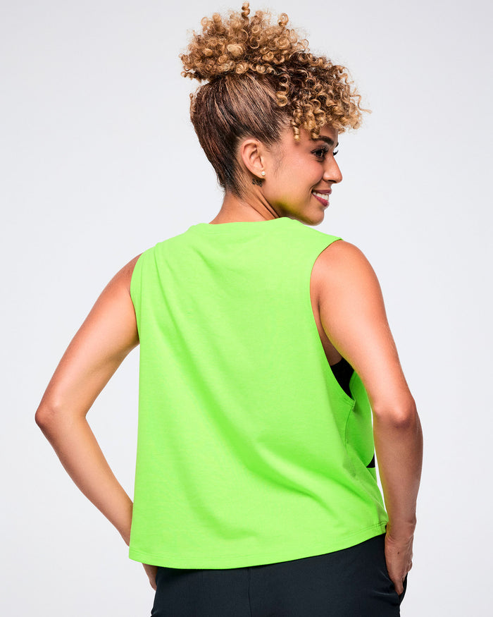 Back view of a female model wearing a neon green sleeveless Zumba tank and black pants on a white background.