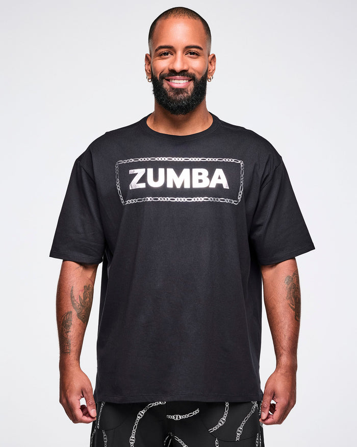 Male model wearing a black Zumba T-shirt with “ZUMBA” in a silver patterned rectangle, paired with matching pants.