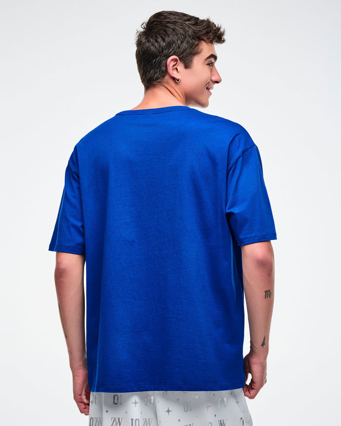 Back view of a male model wearing a blue Zumba t-shirt on a white background.