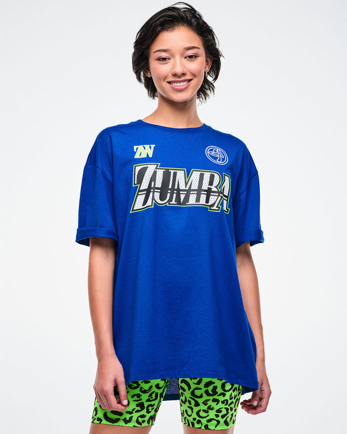 Female model wearing a blue Zumba t-shirt on a white background.
