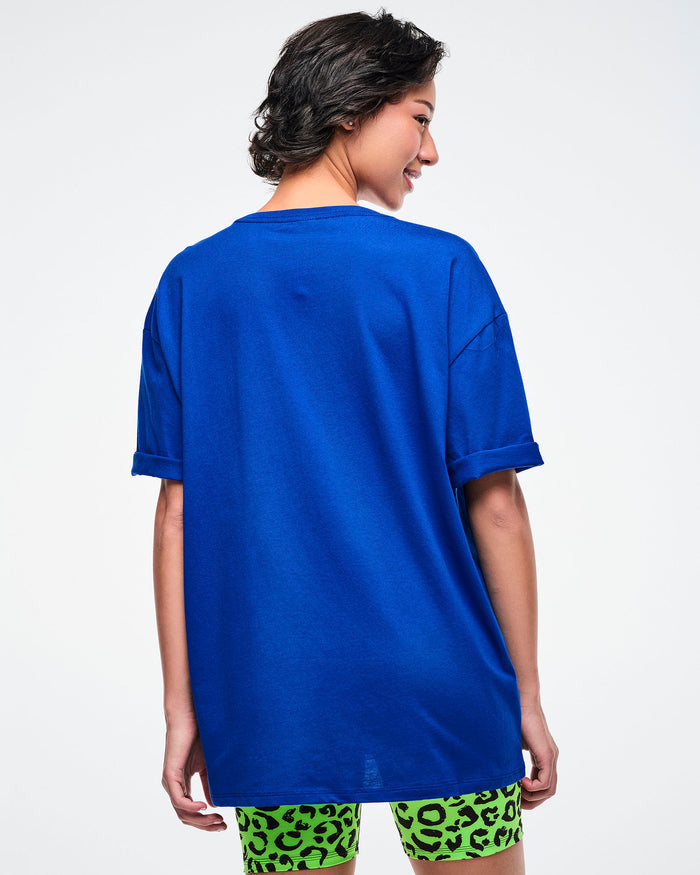 Back view of a female model wearing a blue Zumba t-shirt on a white background.