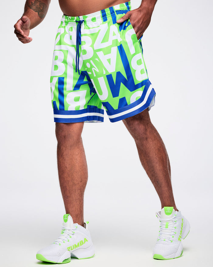Male model wearing green, blue and white patterned ZUMBA lettering shorts paired with green and white shoes.