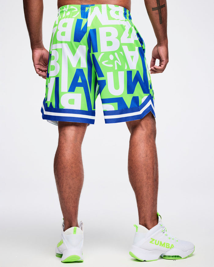 Back view of a male model wearing green, blue and white patterned ZUMBA lettering shorts paired with green and white shoes.
