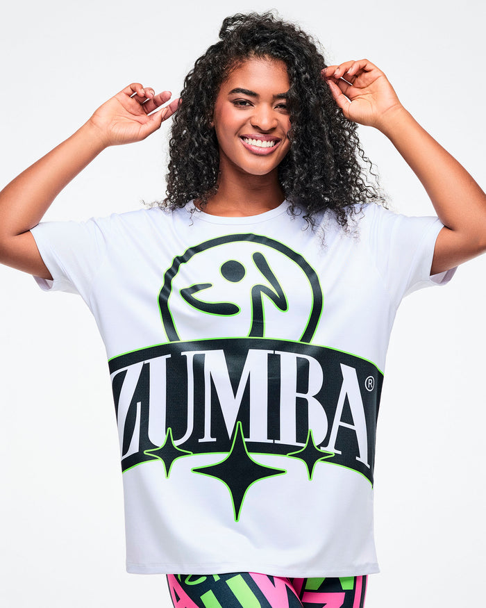 Close-up of a female model in a white Zumba top with a black and green logo.