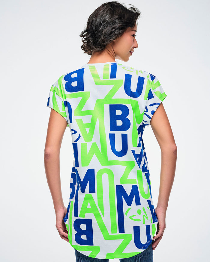 Back view of a female model wearing a colorful t-shirt with "ZUMBA" letter patterns on a plain background.