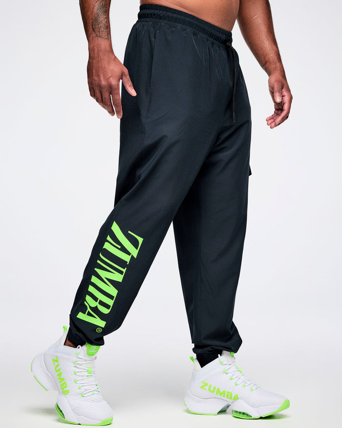Male model wearing black cargo pants with green "ZUMBA" text on the right leg paired with white and green shoes.